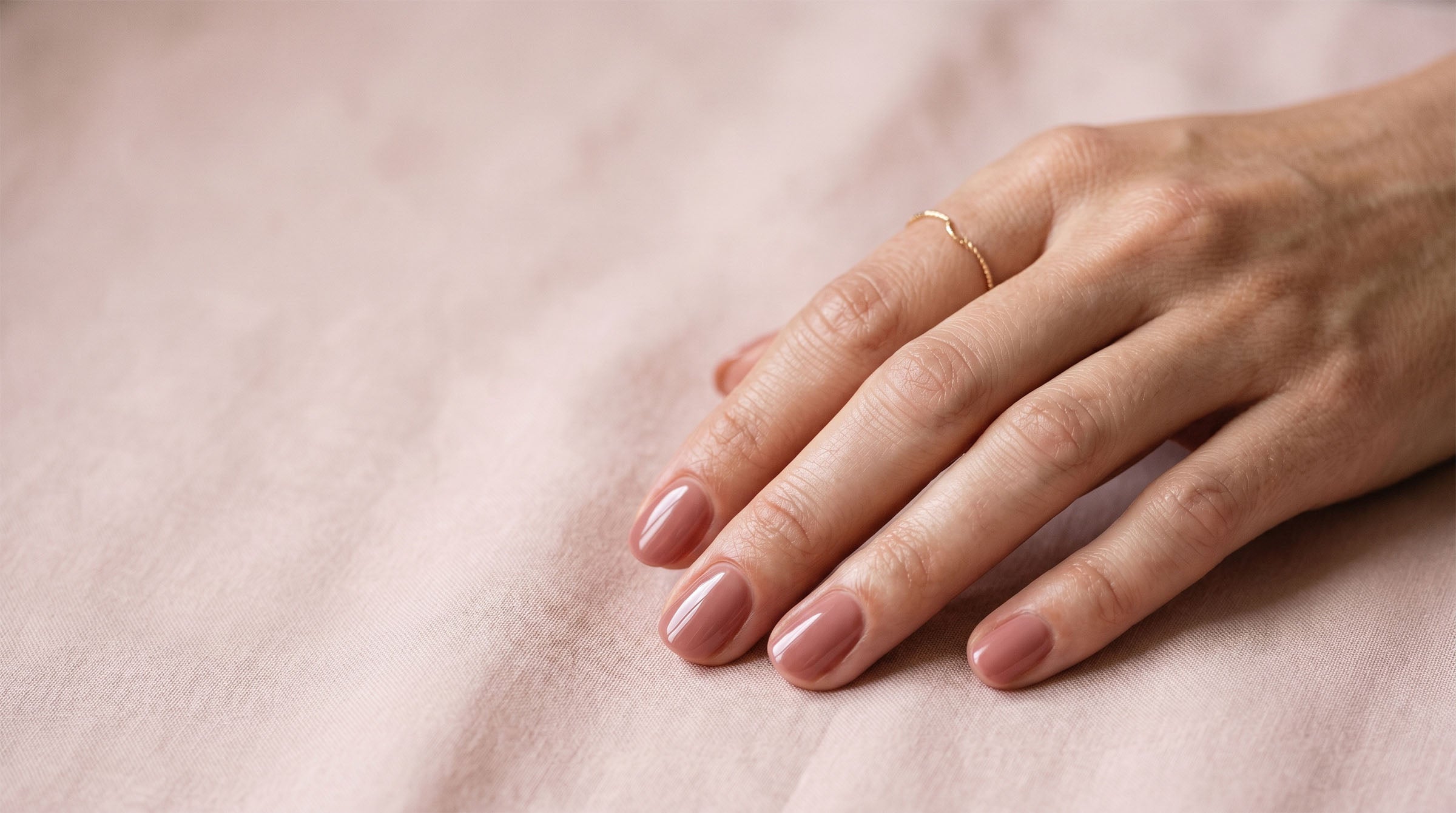 Hand with a glossy rosy-nude Dazzle Dry manicure resting on soft blush fabric